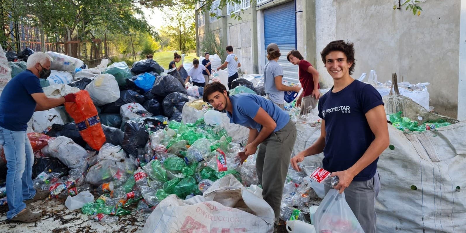 Gente de pie recolectando un gran montón de desechos en un área pública.