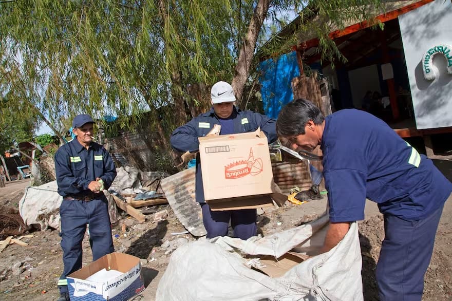 Tres hombres con uniformes azules cargan cajas en un camión.